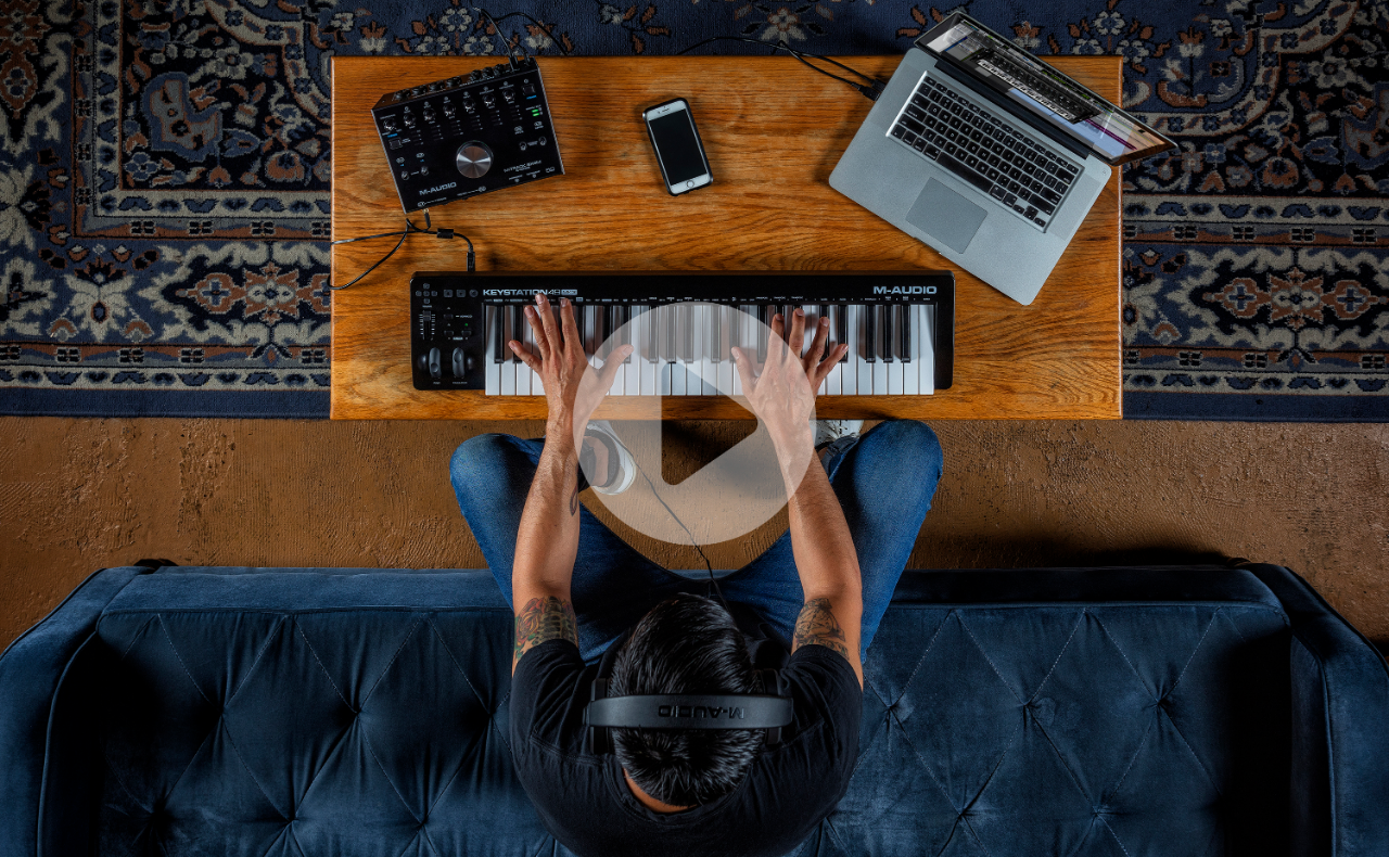 M-Audio公式サイトのKeystation 49 MK3のページ。机の上にノートPCとオーディオインターフェースと49鍵のキーボードを置いて弾いている写真